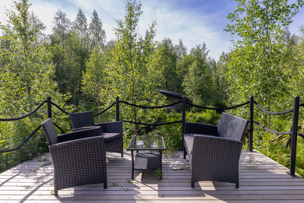 Tummanharmaat puutarhatuolit ja pöytä terassilla vihreiden puiden ympäröimänä, kuva on sivustolta Ylläs Cabins